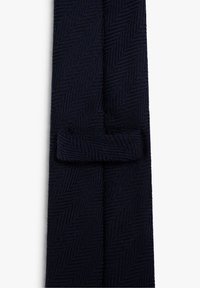 Corbata azul marino con un patrón de espiga, que presenta una tela texturizada. La corbata incluye un lazo de sujeción estrecho para una colocación segura.