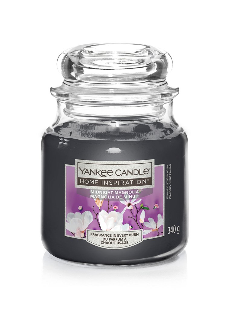 Candela Yankee in un vaso di vetro trasparente con coperchio rotondo. Cera grigia scura. L'etichetta presenta tonalità violacee e illustrazioni di fiori di magnolia bianchi. 340 g.