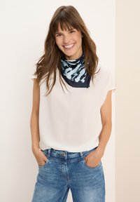 Sciarpa a righe blu navy e azzurro chiaro indossata su una maglietta bianca a maniche corte, abbinata a jeans blu sbiaditi. Tessuto morbido, design casual.