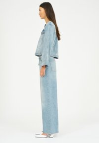 Ljusblå denimjacka med avslappnad passform, kombinerad med lång denimkjol. Vita klackskor med blockklack. Enkelt design, utan synliga mönster.