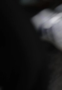 Biely keramický hrnček s hladkým lesklým povrchom, ktorého súčasťou je jednoduchá zakrivená rúčka a zaoblené telo, umiestnený na tmavšom pozadí.