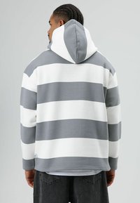 Hoodie met afwisselend grijze en witte strepen. Gemaakt van zachte stof, heeft een relaxte pasvorm en een kangoeroezak.