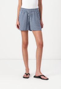 Shorts à carreaux bleu marine et bleu clair, avec une taille élastique. Portés avec des tongs noires, montrant une coupe décontractée et un style casual.