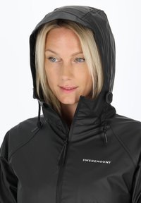 Giacca nera impermeabile con chiusura a zip frontale, cappuccio regolabile e logo decorativo. Tessuto liscio con un design elegante e aderente, senza motivi visibili.