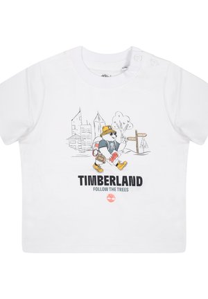 T-shirt blanc à manches courtes avec un graphique de nounours en dessin animé, un chapeau jaune et le texte "TIMBERLAND SUIVEZ LES ARBRES" imprimé en dessous. Tissu en coton doux.