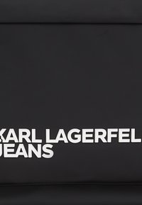 Fekete textúrájú szövet, kiemelkedő fehér bélyegzett szöveggel "KARL LAGERFELD JEANS", középen és vastag betűkkel, további design elemek vagy minták nélkül.