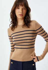 Maglione a coste in beige con strisce blu navy. Design aderente con maniche lunghe e collo rotondo. Il tessuto testurizzato mette in risalto le strisce.