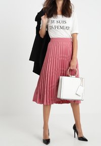 Falda midi plisada rosa combinada con una camiseta gráfica blanca y un blazer negro. Los accesorios incluyen un bolso blanco con un asa redonda y tacones negros.