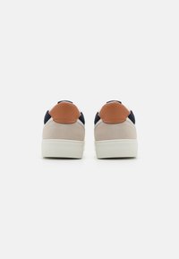 Sneakers with a beige suede body, navy blue accents, and a brown leather heel patch. White rubber soles with textured grip.