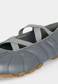 Γκρι παπούτσι τύπου slip-on με ελαστικές λωρίδες που διασταυρώνονται και υφασμένο καφέ λαστιχένιο πέλμα, σχεδιασμένο για καθημερινή χρήση και εύκολη εφαρμογή.