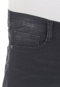 Vaqueros de mezclilla negra con un diseño clásico de cinco bolsillos, costuras resistentes, textura suave y un acabado ligeramente desgastado.
