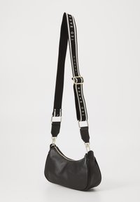 Schwarze Leder-Umhängetasche mit geschwungener Form, goldfarbener Reißverschluss und verstellbarem schwarzen Tragegurt mit weißem Logotext. Glatte Textur mit Akzenten.