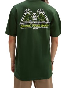 Green cotton t-shirt featuring a graphic of a skull and skeleton hands with turntables, text reading "Sounds From Below," in yellow and white.