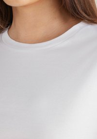 T-shirt bianco in cotone con scollo rotondo. Il tessuto appare liscio con una morbida consistenza, senza modelli o accenti visibili.