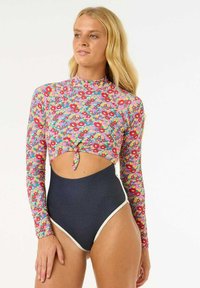 Maillot de bain à manches longues avec un motif floral en rose, rouge et bleu. Découpé à la taille, bas taille haute bleu marine avec bord blanc.