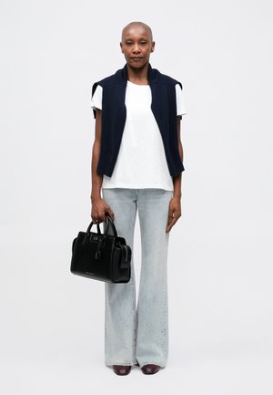 Bolso negro con asas redondeadas, superficie texturizada, combinado con una camisa blanca, un suéter sin mangas azul marino y unos vaqueros acampanados de color azul claro.