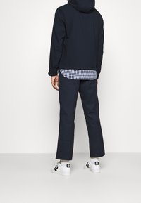 Giacca con cappuccio blu navy, camicia casual a quadri sotto, pantaloni scuri e sneakers bianche. Design semplice con linee pulite e colori a contrasto.