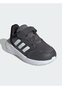 Šedé tenisky vyrobené z meshového a koženého materiálu, s páskem na suchý zip, třemi bílými pruhy po straně, zaoblenou špičkou a bílou gumovou podrážkou.