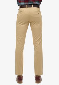 Chino beige con vestibilità slim, caratterizzati da una texture liscia, tasche posteriori, cuciture sottili e una cintura marrone in vita.