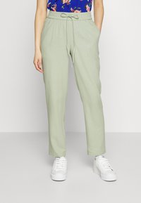 Jasnozielone, luźne spodnie z elastycznym pasem i sznurkiem. Połączone z białymi trampkami. Gładki, lekki materiał.