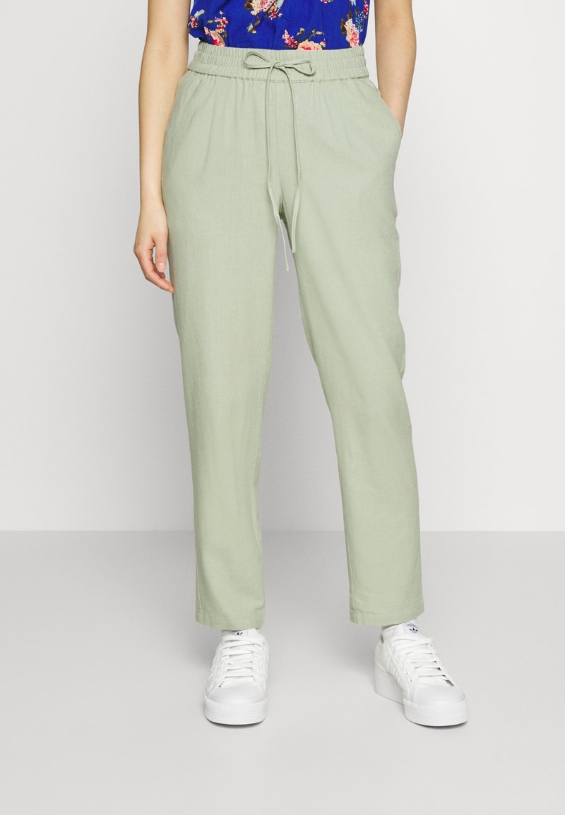 Jasnozielone, luźne spodnie z elastycznym pasem i sznurkiem. Połączone z białymi trampkami. Gładki, lekki materiał.