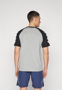 Grå kortermet t-skjorte med svarte raglan-ermer, med hvite detaljer, rund hals og glatt stoffstruktur, brukt sammen med marineblå shorts.