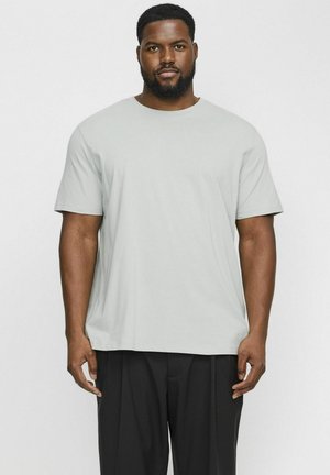 Lichtgrijs T-shirt met korte mouwen van zachte stof, met een relaxte pasvorm en ronde hals. Gecombineerd met donkere geplooide broeken.