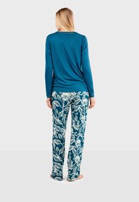 Haut à manches longues teal associé à un pantalon large à motifs floraux en bleu foncé et blanc. Tissu doux, coupe décontractée, sans accents visibles.