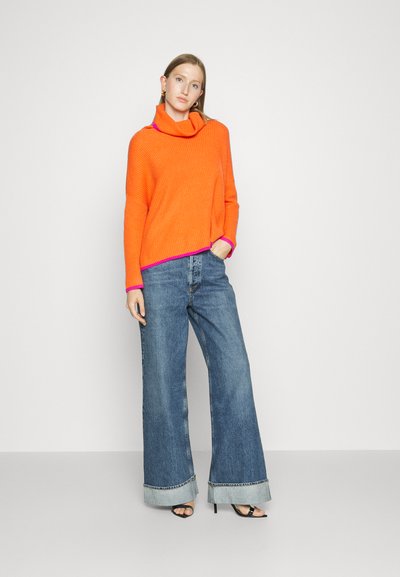 Bright orange ribbed sweater with a cowl neck and purple accents, paired with wide-leg blue jeans featuring hemmed cuffs.