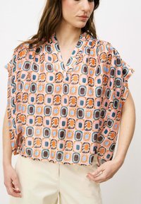 Kurzarmbluse aus leichtem Material mit einem mehrfarbigen geometrischen Muster, das Quadrate in Orange-, Blau- und Brauntönen zeigt.