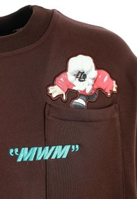 Sudadera marrón con un personaje de dibujos animados bordado en rojo y blanco. "MWM" bordado en azul claro en el bolsillo delantero. Textura suave.