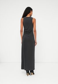 Maxi haljina od tamnosive tkanine, bez rukava s nabranim detaljem na leđima, glatke teksture, uparena s crnim visokim potpeticama.