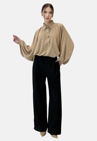 Beige, oversized overhemd met brede mouwen, gecombineerd met losse zwarte broeken en beige puntige hakken. Gladde stof, minimalistisch ontwerp.
