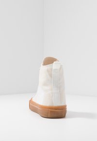 Vita högskor med en texturerad tygöverdel, beiga detaljer och en ljusbrun gummisula. Har en dragflik vid hälen.