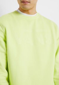 Jasnozielony sweatshirt z okrągłym dekoltem, z delikatnym wytłoczonym logo "VANS" na klatce piersiowej. Miękka tekstura i luźny krój.