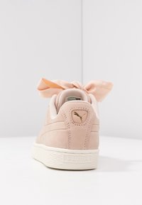 Baskets en daim rose avec une semelle en caoutchouc crème, ornées d'un grand nœud en satin sur le talon et d'un logo doré. Texture lisse.