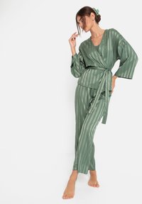 Set van groene gestreepte zijde loungewear met een wikkeltop met een strikceintuur en bijpassende taps toelopende broek met zijsplitten, die het elegante ontwerp benadrukken.