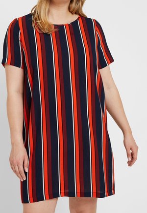 Femme portant une robe à manches courtes avec des rayures verticales bleu marine, rouge, bordeaux, orange et blanc sur un fond uni.