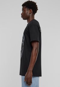 Black cotton t-shirt with short sleeves, featuring a graphic print on the front and a crew neckline, straight hem, and relaxed fit.