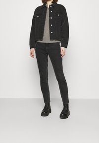 Schwarze Denimjacke mit Kragen, silbernen Knöpfen, zwei Vordertaschen, kombiniert mit schwarzen engen Jeans und klobigen schwarzen Schnürstiefeln.