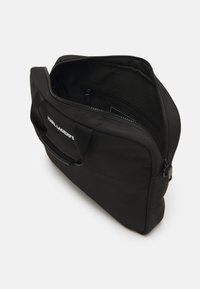 Svart laptopveske med glidelås, med topphåndtak og tekstilstruktur. Inkluderer en innvendig lomme og en logoåndrakk på forsiden.