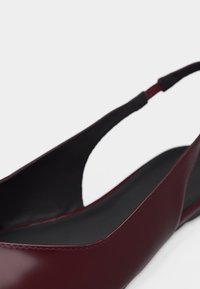 Μπαλαρίνα slingback σε μπουρντό χρώμα με λείο φινίρισμα, μαύρη εσωτερική σόλα και ελαστικό λουρί στο πίσω μέρος για σταθερή εφαρμογή.