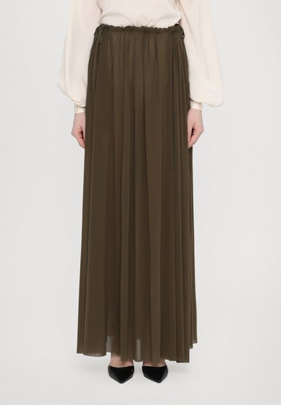 Falda maxi en verde oliva, hecha de un tejido fluido y ligero con un diseño plisado. Cintura elástica, combinada con zapatos de punta negros.