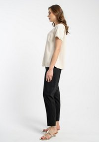 Beżowa bluzka z krótkim rękawem, ozdobiona koronką, w połączeniu z czarnymi spodniami i srebrnymi sandałami na obcasie. Gładki materiał o luźnym kroju.