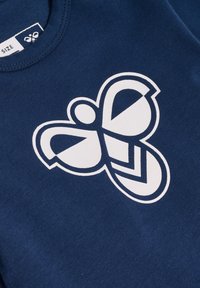 Mörkblå t-shirt med en stor vit fjärilsgrafik, med geometriska mönster och mjuk tygtextur. Storleksmärke fäst.