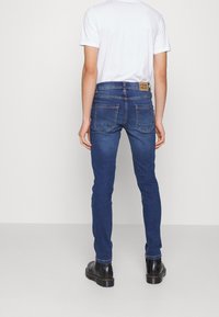 Blå denim skinny jeans med medelhög midja, två bakfickor, brun läderlapp vid midjan och slim-fit design.