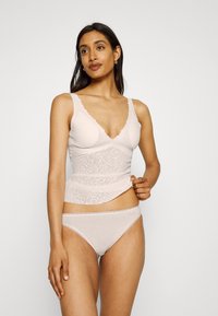 Világos rózsaszín csipke camisole, fodros szélekkel és mély V-kivágással, hozzáillő könnyű bikininadrággal párosítva. Az anyag sima tapintású.