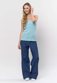 Šviesiai mėlynas siaurai briaunuotas tankinis marškinėlis derinamas su laisvai krentančiais tamsiai mėlynos spalvos džinsais ir baltais sportiniais bateliais, pateiktas ant paprastos baltos fono.