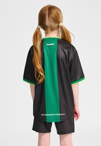 Svart sporttröja med vertikal grön rand, korta ärmar och gröna detaljer. Har "hummel"-logotyp och texten "INTERNATIONALS" på baksidan.