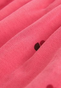 Różowy materiał o miękkiej teksturze, z ciemnobrązowymi groszkami w powtarzającym się wzorze, ułożonym w poziome fałdy.